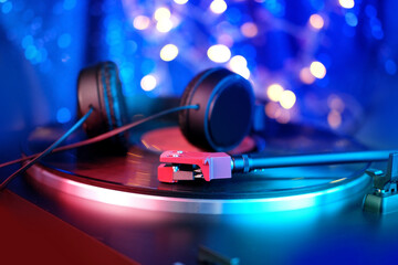 close-up of a pickup head, black headphones on a vinyl record, colored lights, analogue retro music...