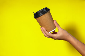 Close-up on a yellow background, a woman's hand holds a paper cup with coffee in a stand. Coffee or tea with you, coffee delivery on a yellow background