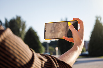 Screen view of young woman with yellow painted nails taking selfie at golden hour