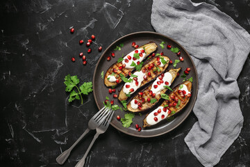 Grilled eggplants with yoghurt sauce and pomegranate on a black stone background. Top view, flat...