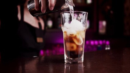 bartender pours a cocktail from shaker into a glass of ice