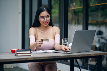 Portrait of Cute woman holding white credit card for shopping online with computer while sitting in...