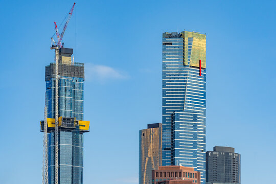 Horizontal shot of two high rise building, one under construction in front of a clear blue sky