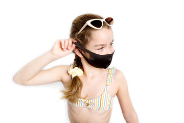 Naklejka premium Happy little girl takes off her covid-19 protective medical black mask from her face in a beach suit outdoors. The concept of defeating the coronavirus.