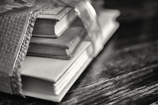Black and white image of well read and worn out books wrapped with a hemp and gold ribbon on an antique wooden floor