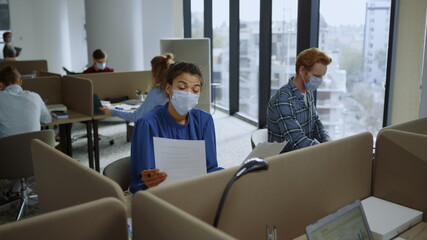 Businesswoman looking at documents. Professionals in masks talking in office