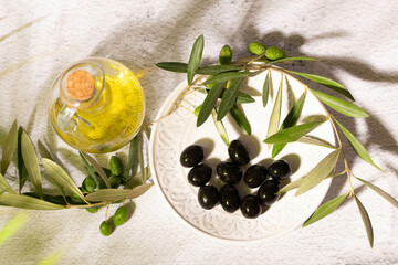 A glass jar with virgin olive oil, textured plate with black olives and a branch of olive tree