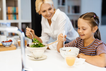 White mother and daughter smiling while having lunch in kitchen at home