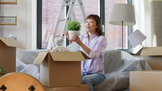 moving, people and real estate concept - happy smiling asian woman unpacking boxes at new home