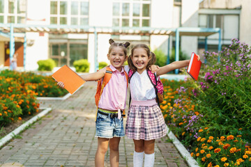 Two girls, elementary school students with backpacks, walking down street Happy children are returning to school. beginning of school year. Children in full growth, happily went to school. rear view