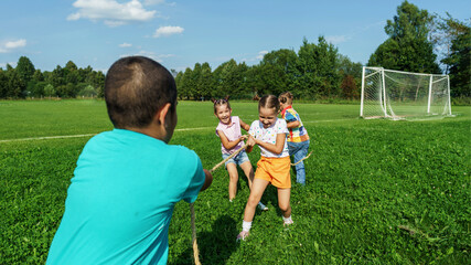 group of small happy preschool children play tug of war in the park on a sunny summer day. Outdoor...