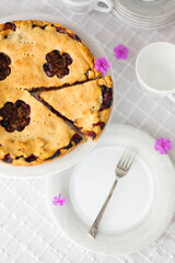 Rhubarb or pieplant and blueberry pie surrounded by white porcelain dishes and violet phlox flowers on white tablecloth