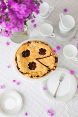 Rhubarb or pieplant and blueberry pie surrounded by white porcelain dishes and violet phlox flowers on white tablecloth