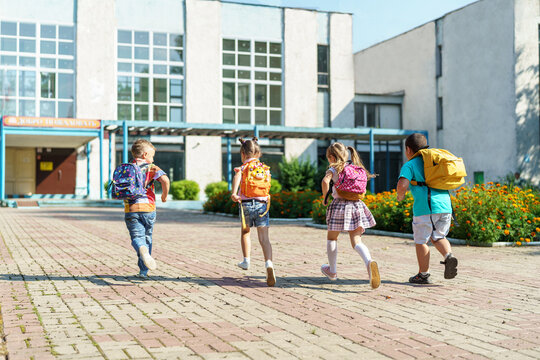 group of school children with backpacks run out of school, after the end of classes. Classmates, school friends. The beginning of holidays. The end of quarantine. Back to school.