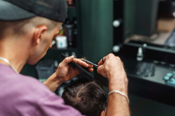 young barber guy gives a haircut to a bearded man sitting in a chair in a barbershop. A man cuts his hair with scissors and a comb. Men's haircuts and beard shaving. Haircut and edging of eyebrows.