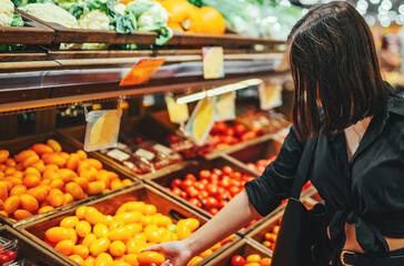 Woman chooses and purchases fresh ripe organic tomatoes in vegetable department of supermarket