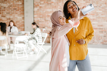 Multiracial two women taking selfie photo on cellphone during meeting