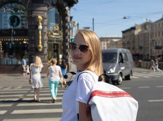 A beautiful girl-guide, blonde, in a white T-shirt, with a backpack, in the afternoon on a city street.