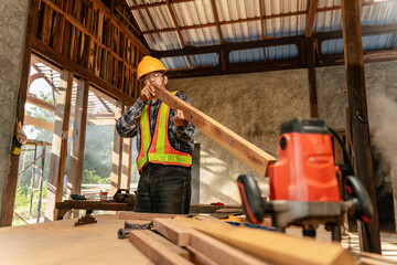 Fototapeta na wymiar Attractive hardworking middle aged professional male carpenter worker looking and choosing wood on wooden table at construction site.