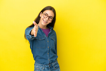 Young French woman isolated on yellow background shaking hands for closing a good deal