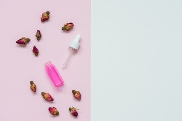 top view of dried rose buds and rose essential oil in a transparent pink glass bottle.on a...