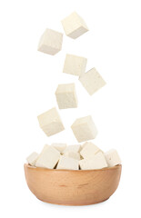 Cubes of raw tofu falling into bowl on white background