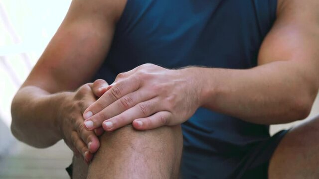 fitness, sport and health concept - young man massaging injured leg or knee outdoors