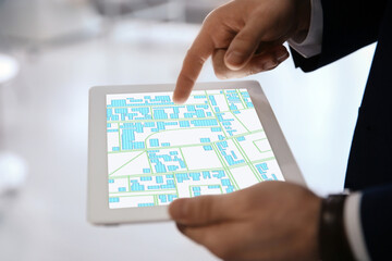 Man analyzing cadastral map on tablet indoors, closeup
