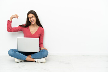 Young French girl sitting on the floor with her laptop doing strong gesture