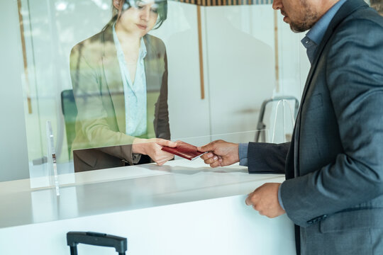 Unrecognizable Businessman Handing Over Passport to Hotel Receptionist.
An anonymous business man passing documents to woman concierge on hotel reception with sneeze guard protection. 