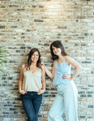 Portrait of Two Smiling Friends Standing Against the Brick Wall Together.
Two beautiful woman looking at camera and standing confident over the brick wall.