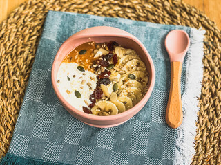 Porridge, oatmeal, oat bowl, banana, peanut butter, raisins, seeds, healthy breakfast for kids, babies, silicone baby bowl, toddler bowl, pink tableware, teal napkin, rattan placemat, silicone spoon