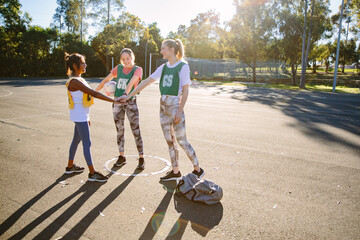horizontal shot of three young smiling women in sports clothes stacking hands on top of each other