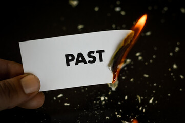 burning past, human hand holding the word past written on a paper burning with flame and ashes on a...