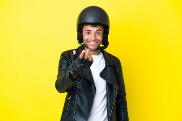 Young Brazilian man with a motorcycle helmet isolated on yellow background inviting to come with hand. Happy that you came