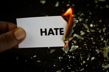 burning hate, human hand holding the word hate written on a paper burning with flame and ashes on a...