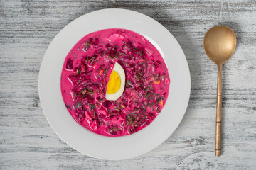Delicious cold summer beetroot soup with cucumber, boiled egg, radish in white plate on table