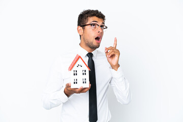 Young business Brazilian man holding a house toy isolated on white background thinking an idea pointing the finger up