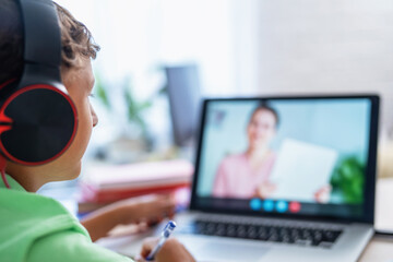 little boy with headphones is using laptop to make video call with his teacher. screen displays online lecture with teacher explaining subject from class. E-Education Distance Learning, Home Schooling