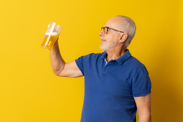 Old man drink beer isolated over yellow background.