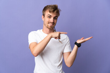 Young handsome blonde man isolated on purple background holding copyspace imaginary on the palm to...