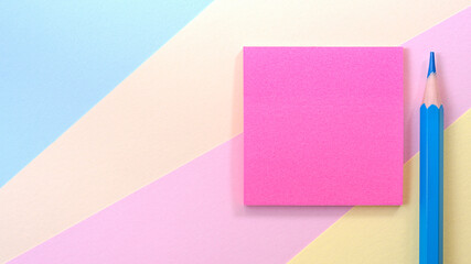 A pink square blank piece of paper lies on a multi-colored background, next to it lies a blue pencil.