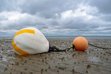 Orange und gelbweisse Warnboje im Watt vor Cuxhaven Sahlenburg mit Wattwurmhaufen bei Ebbe