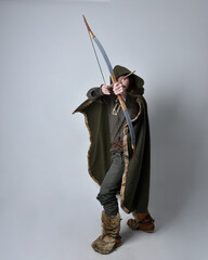 Full length  portrait of  young handsome man  wearing  medieval Celtic adventurer costume with hooded cloak, holding a archery bow and arrow, isolated on studio background.