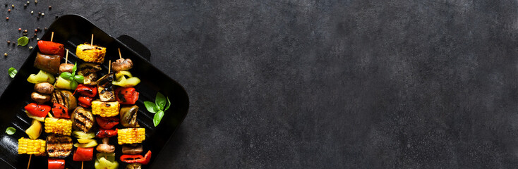 Vegetable skewer on a skewer in a grill pan on black concrete background. Vegetables to grill in a pan.