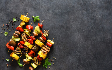 Naklejka na ściany i meble Grilled vegetables on a skewer on a black concrete background. Corn, eggplant, pepper. View from above.
