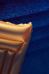 Golden swimming mattress in the pool against blue water on sunset. Vacation and holidays concept photo. Free space. Closeup view from above. Vertical photo.
