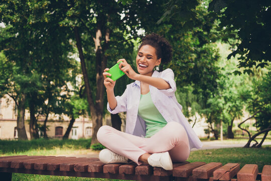 Full size photo of cheerful positive young afro american woman hold phone play game outdoors outside park