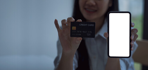 Young woman is showing credit card and smart phone to buy product online from the website on internet, e-commerce and online shopping, financial transaction