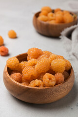 Ripe yellow raspberries. Fresh ripe berries in a wooden plate on a light background